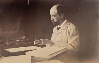 Henry Adams seated at desk in study, writing, in light coat Photograph