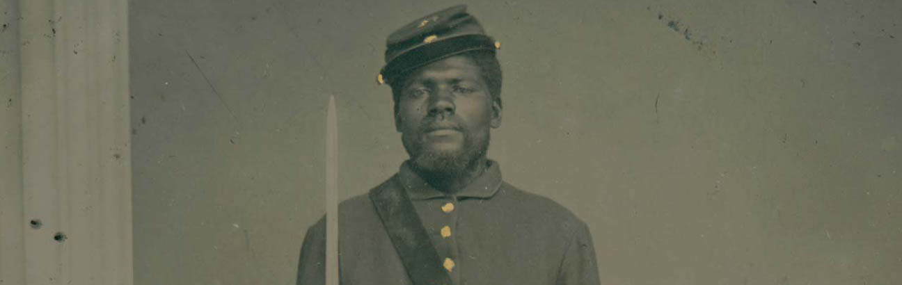 Black and white photo of Black soldier standing at attention holding a sword next to a column