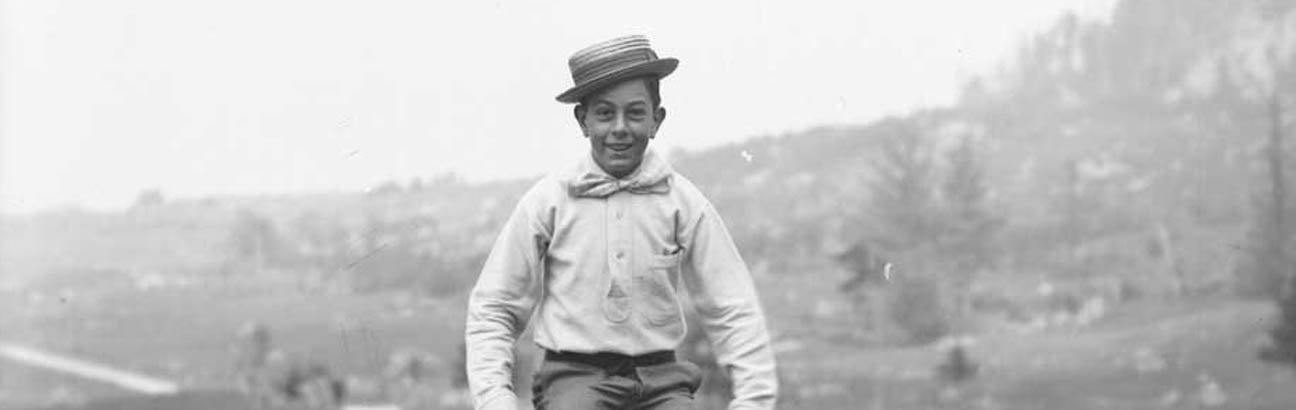 Black and white photo of a young white boy outdoors in mid-jump with his legs tucked under him